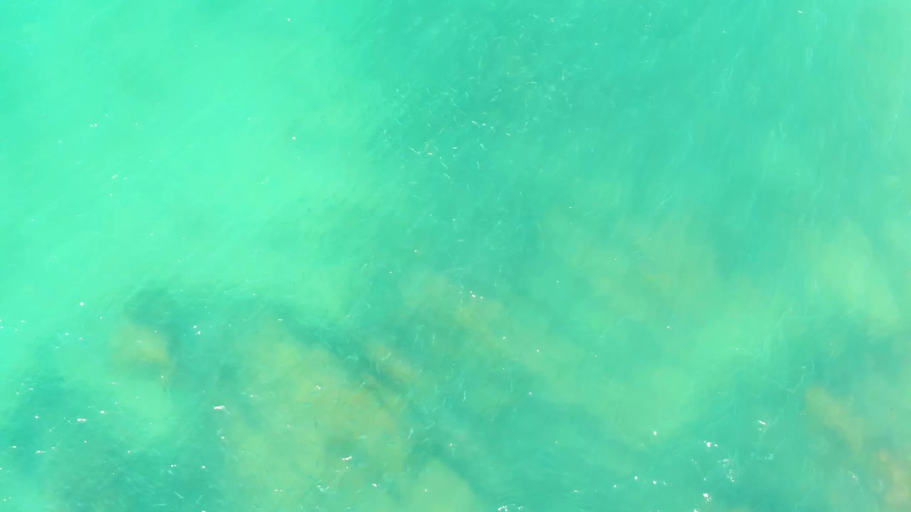 Green-blue shallow seawater at El Tule Beach Los Cabos shows darker underwater rock shapes slightly left of center and no visible people.
