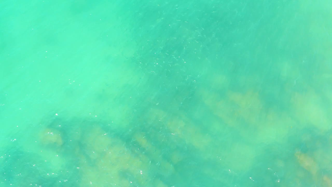 Turquoise shallow ocean water at El Tule Beach Los Cabos contains cloudy submerged rock forms and scattered surface sparkle, with no visible people.