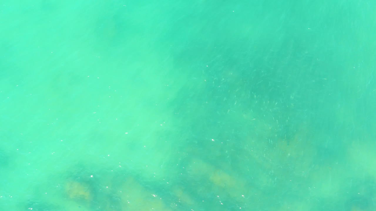Shallow turquoise water at El Tule Beach in Los Cabos passes over cloudy tan rock forms on the seabed, with no visible people or objects.