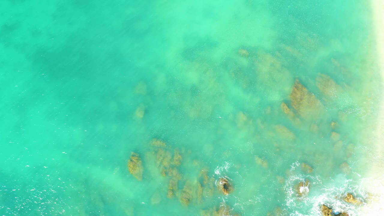 Turquoise shallow water with submerged rock shapes and foam below.