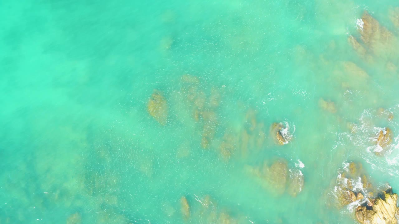 Aerial frame of El Tule Beach Los Cabos water, showing pale sand patches, submerged rock shapes, and no clearly visible people.