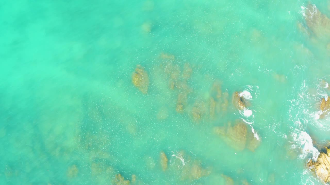 Aerial view over El Tule Beach Los Cabos where turquoise water softens the view of rocks below, with no clearly visible people.