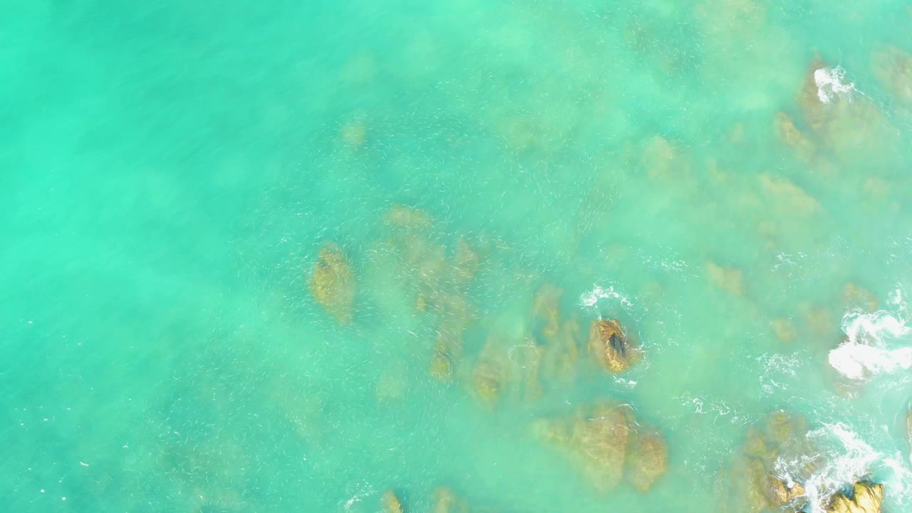 Clear turquoise water with submerged rocks and faint wave texture.