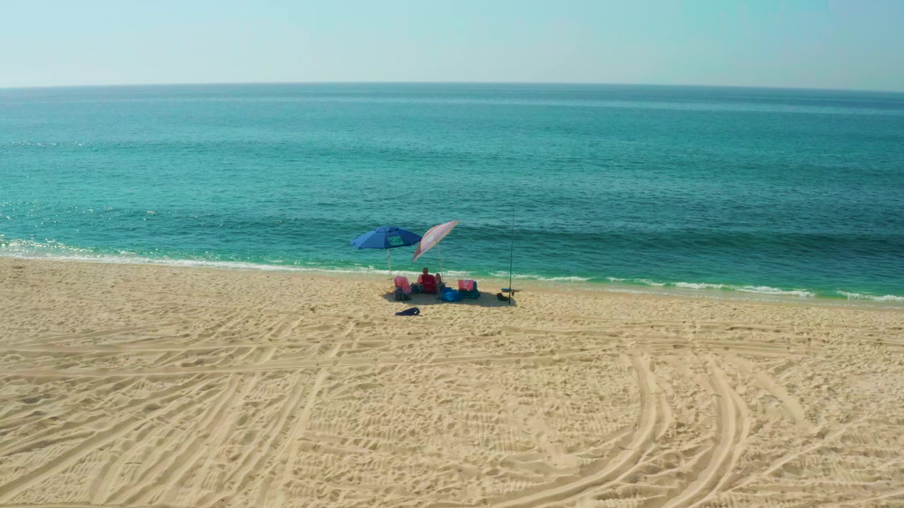 Beach umbrellas, seated people, fishing rods, sand tracks, and calm ocean.