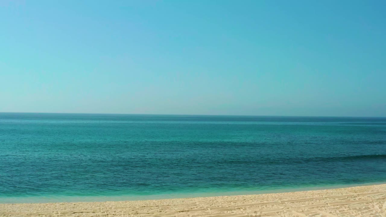 Opening view of El Tule Beach in Los Cabos with a level horizon, blue sky, turquoise water, pale sand at the bottom edge, and no visible people.