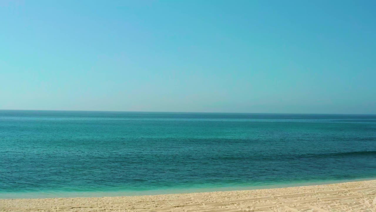 Calm turquoise water and sandy shore under a clear blue sky.