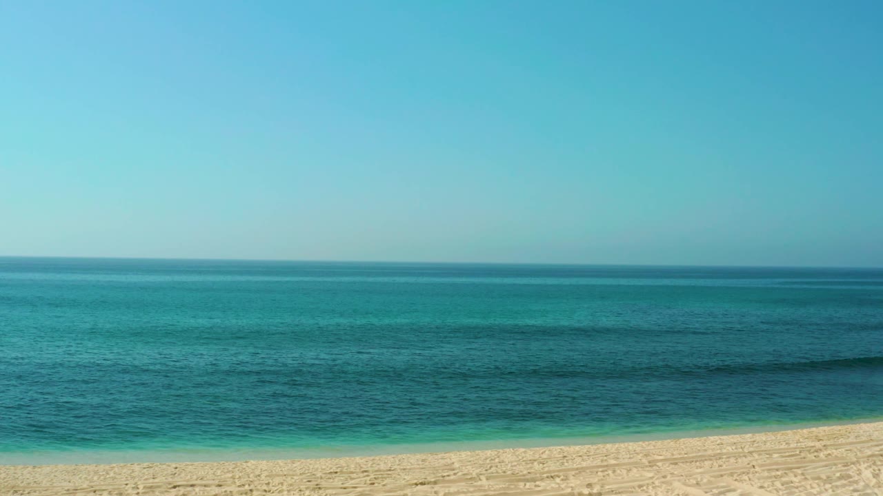A wide El Tule Beach view shows turquoise water meeting a pale sandy shore beneath an open blue sky, with no visible people or buildings.