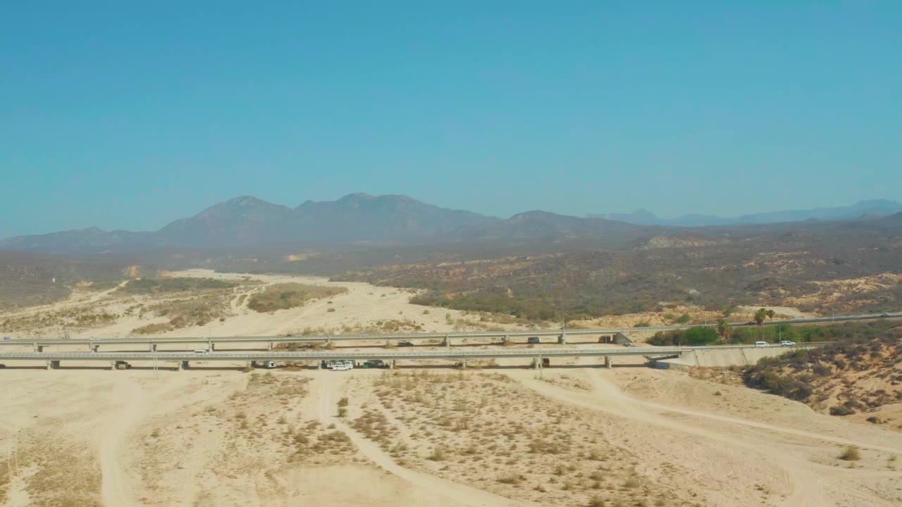 Wide aerial frame of road traffic crossing sandy desert terrain.
