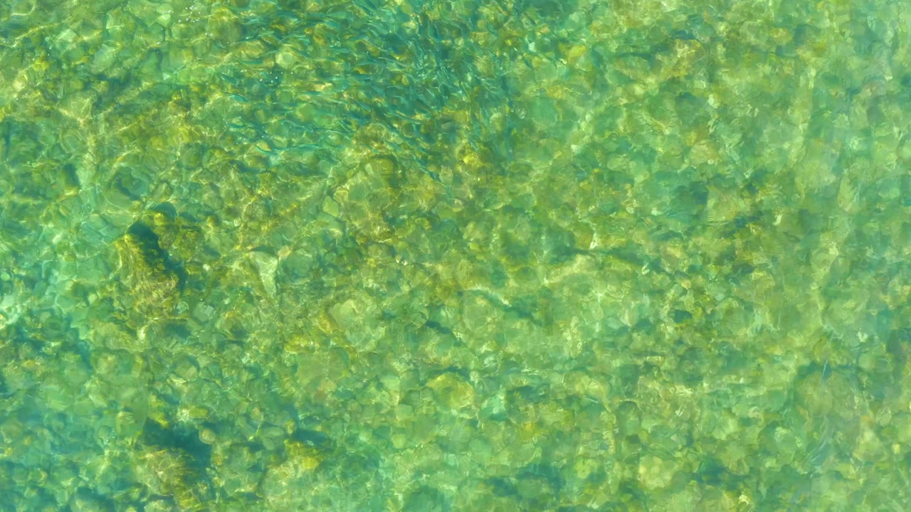 Rippling clear water at El Tule Beach Los Cabos passes over pale underwater rocks and darker submerged patches, with no visible people.