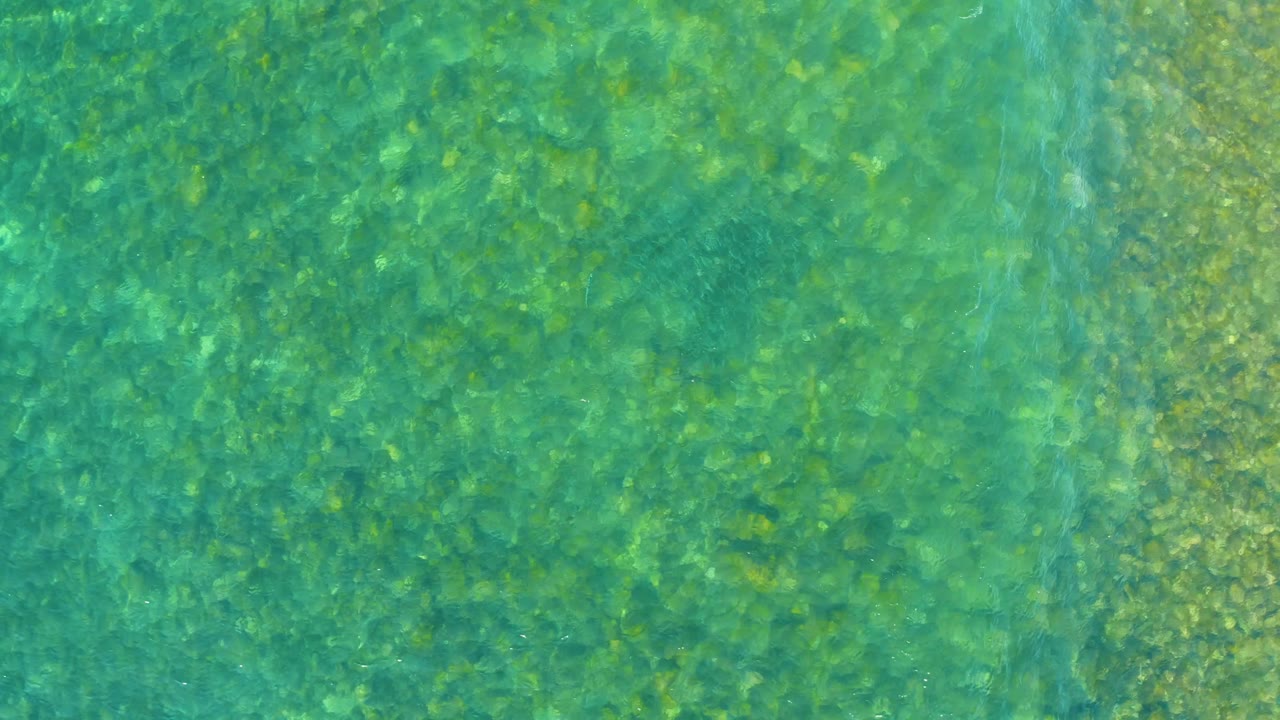 Clear shallow water at El Tule Beach in Los Cabos fills the frame, with the rocky bottom visible through blue-green water and no visible people.