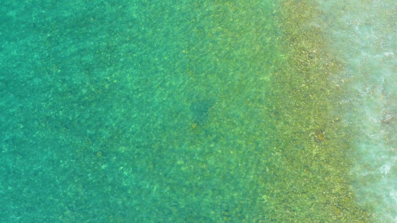 Shallow turquoise water over mottled sand appears at El Tule Beach in Los Cabos, with a faint pale wave band near the right side and no visible people.