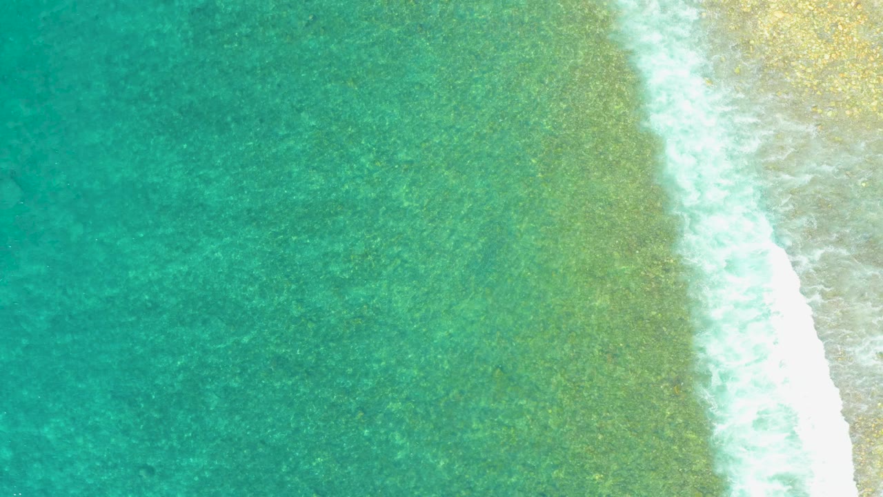 Turquoise shallow ocean water with white surf beside sandy shore.