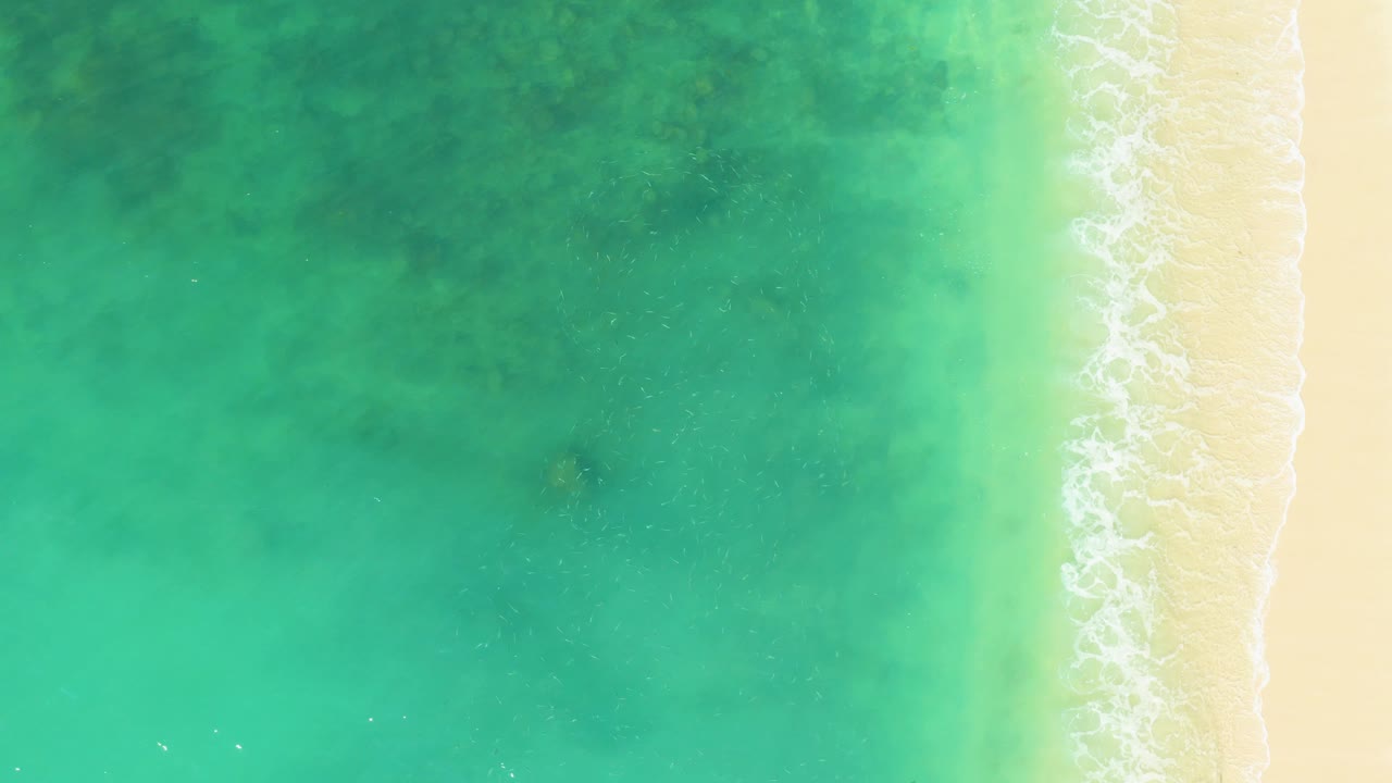 Clear turquoise ocean with foam touching sand at right