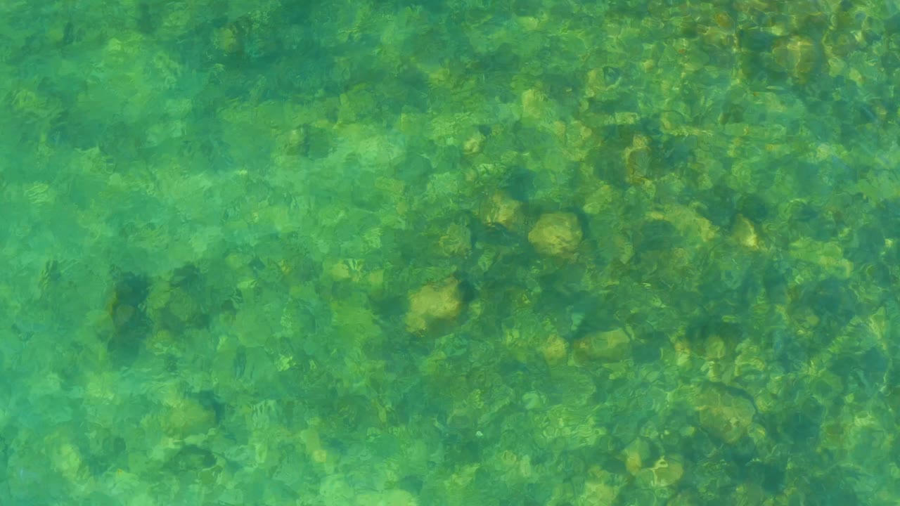 Gentle ripples pass across shallow El Tule Beach water, exposing a pebble and rock bottom with no visible people.