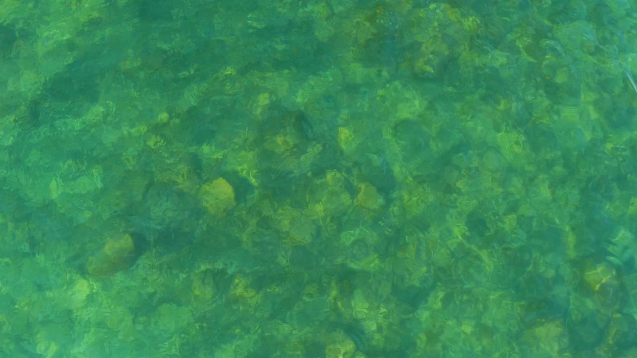 Clear green-blue water at El Tule Beach Los Cabos ripples over a rocky bed with no visible people.