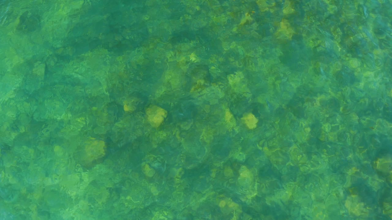 Green-blue water at El Tule Beach Los Cabos covers a field of submerged rocks as surface movement softens their edges, with no visible people.