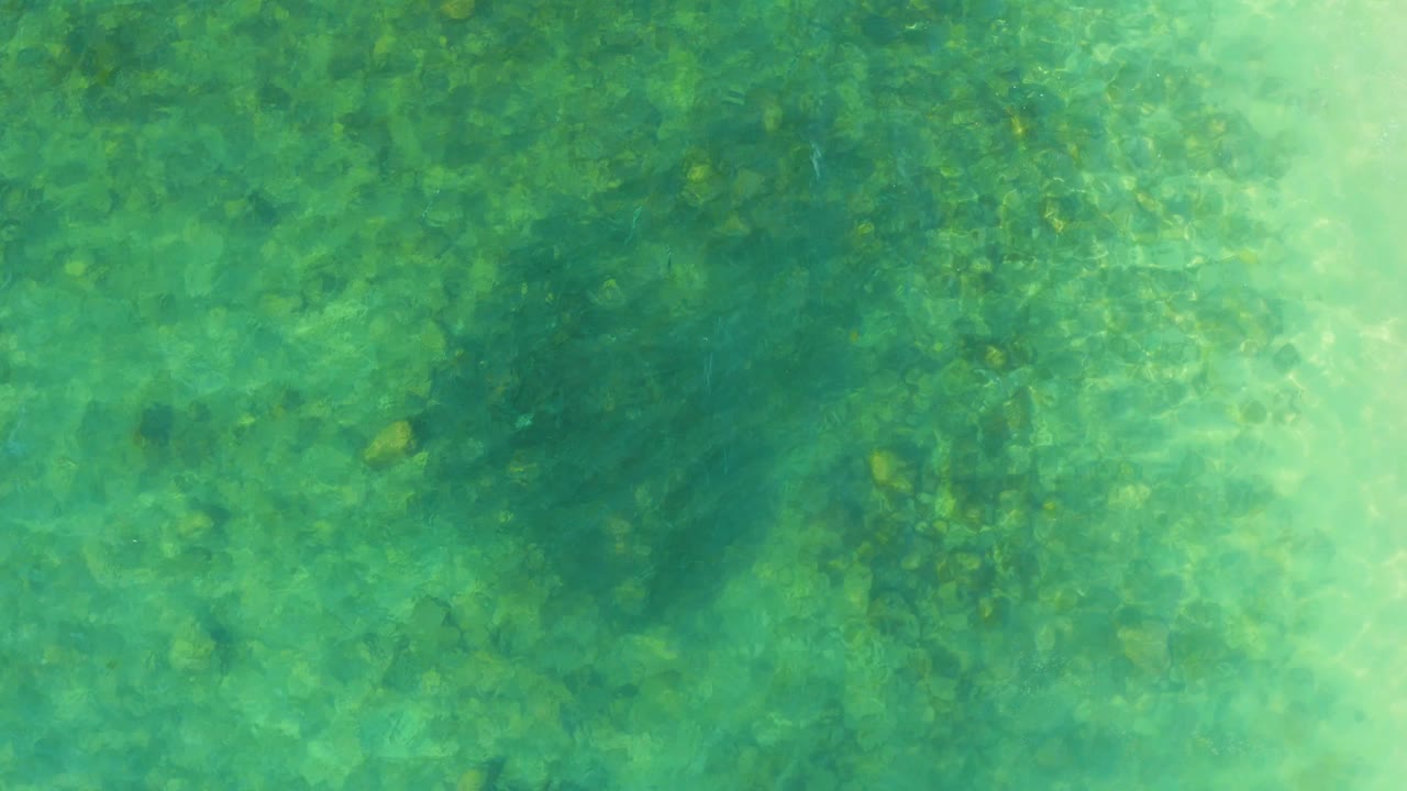 Clear green-blue water at El Tule Beach Los Cabos shows darker patches below the surface and no visible people.