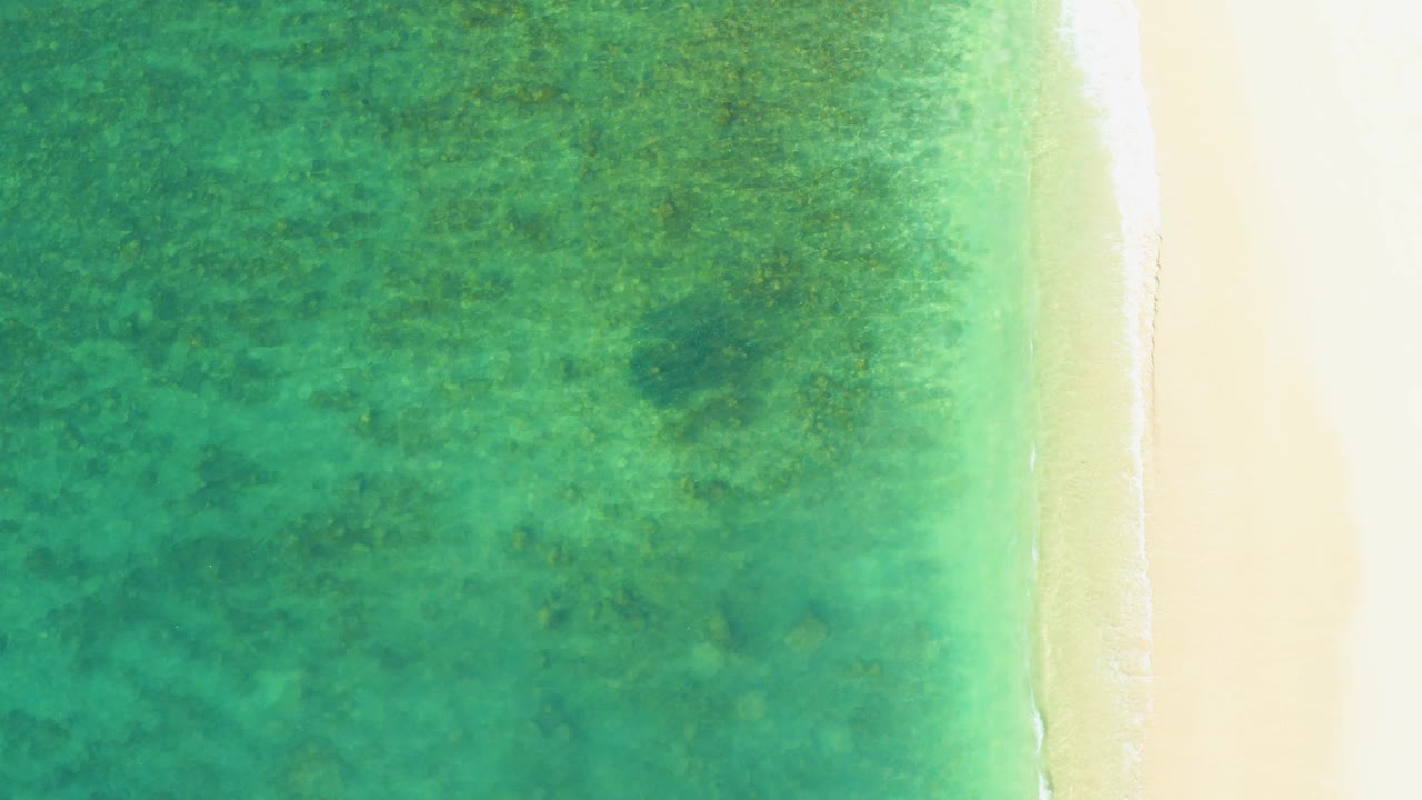 Overhead view of turquoise water meeting pale sand at El Tule Beach in Los Cabos, with a thin surf edge and no visible people.