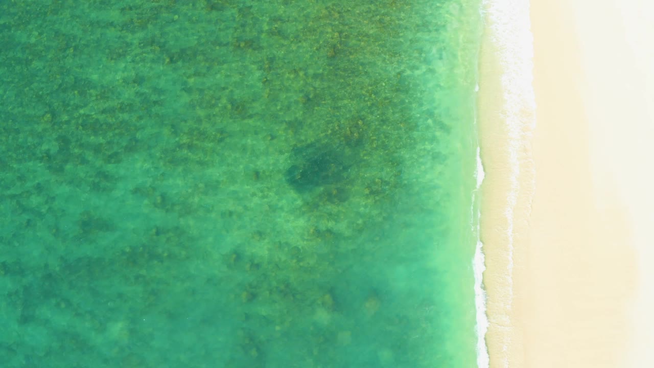 Top-down view at El Tule Beach with turquoise ocean on the left, pale sand on the right, and a brighter white wave edge with no visible people.