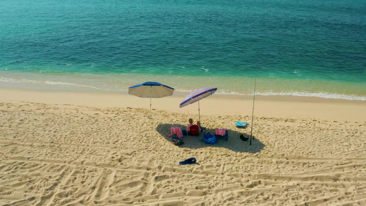 At El Tule Beach in Los Cabos, the third frame shows the beach setup shifted within the aerial composition, with umbrellas, chairs, visible people, and turquoise water above.