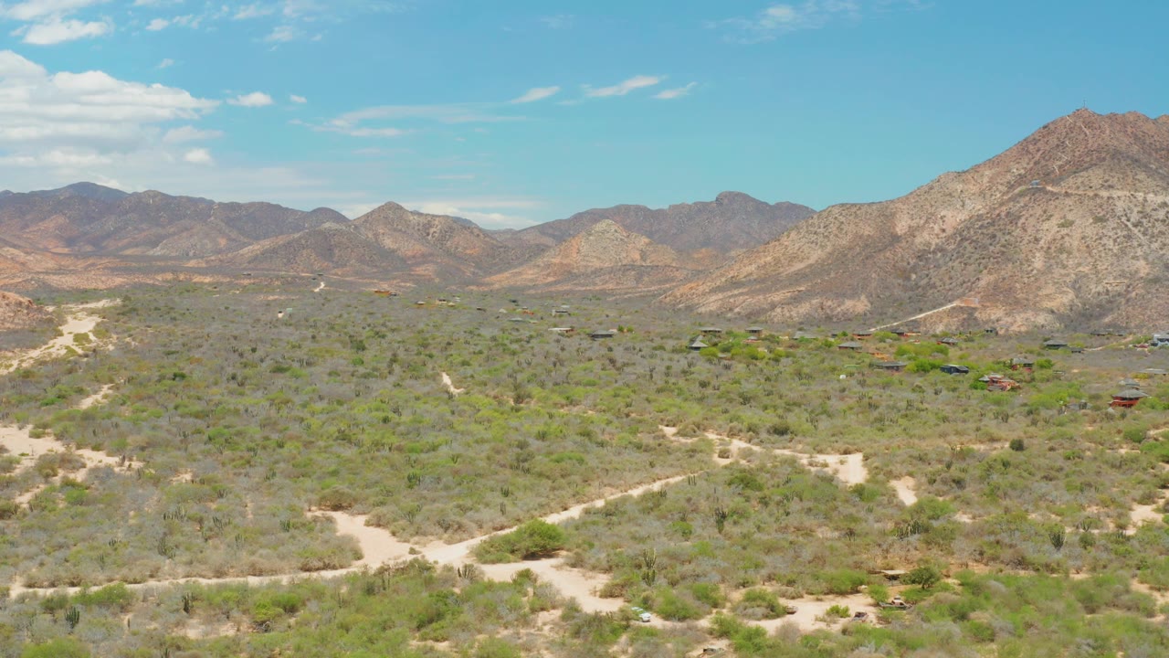At two seconds, the aerial view shows scrubland stretching toward layered rocky hills, with a pale road bending through the lower frame and no visible people.