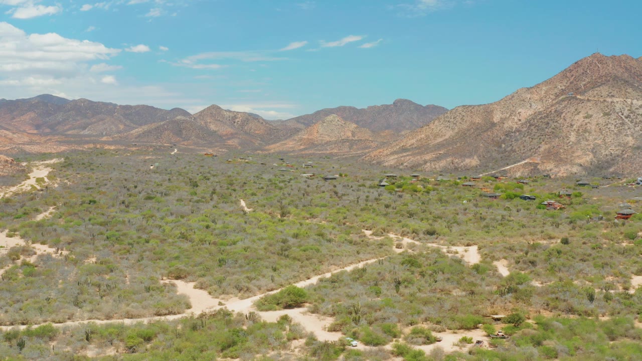 Wide desert aerial with mountains and scattered small structures.