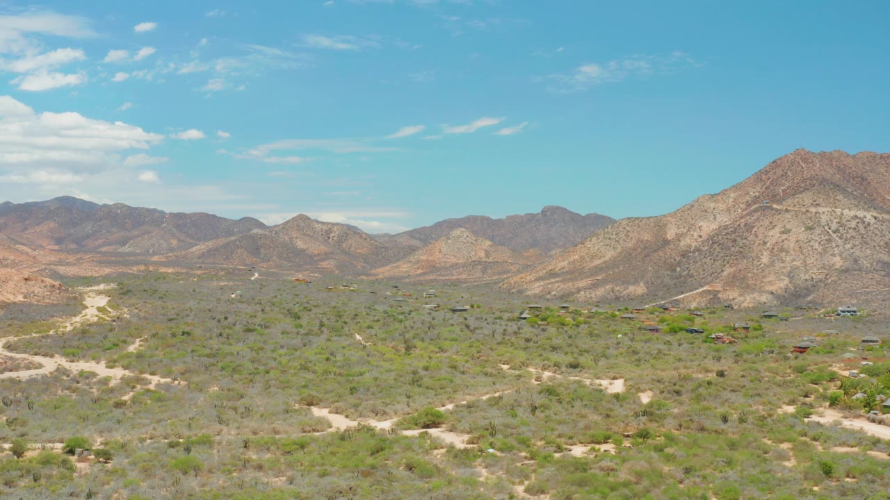 Wide aerial view of scrubland, winding dirt tracks, and mountains