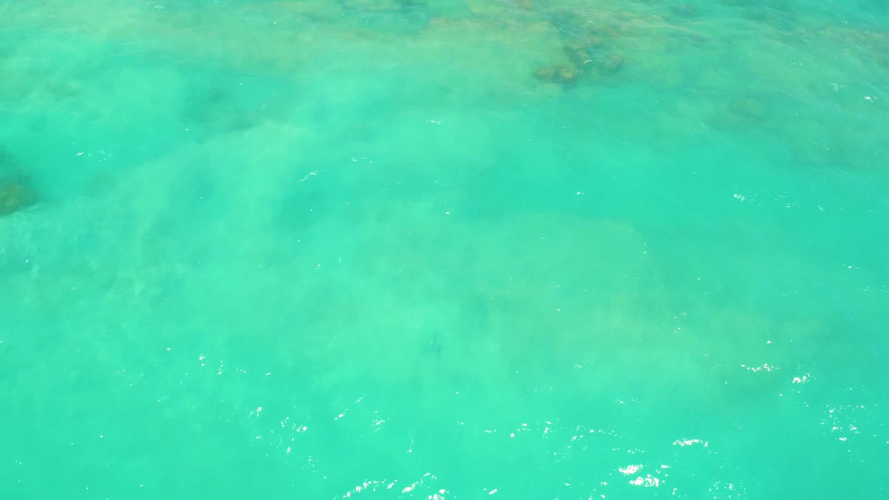 Shallow turquoise sea in Cabo Pulmo fills the frame, with faint sandy seabed, light ripples across the surface, darker underwater patches, and no visible people.