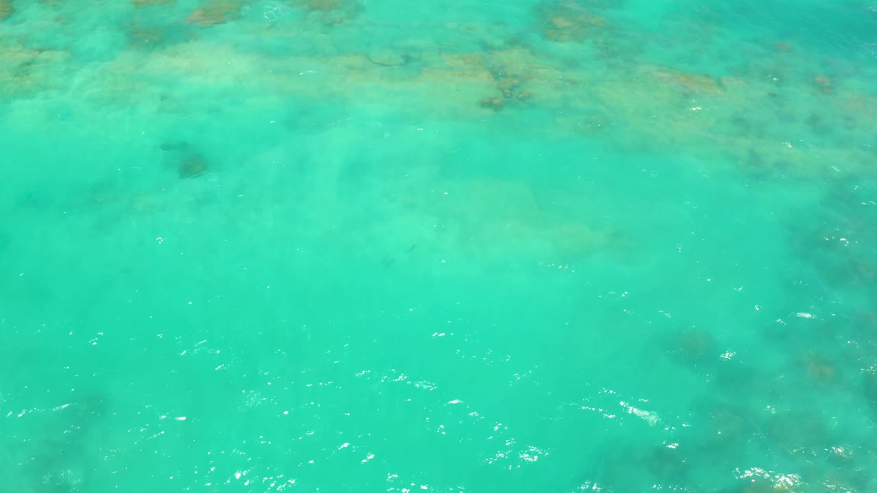 A bright overhead view of Cabo Pulmo shallow water shows faint rocks or coral below the surface and scattered white reflections, with no visible people.