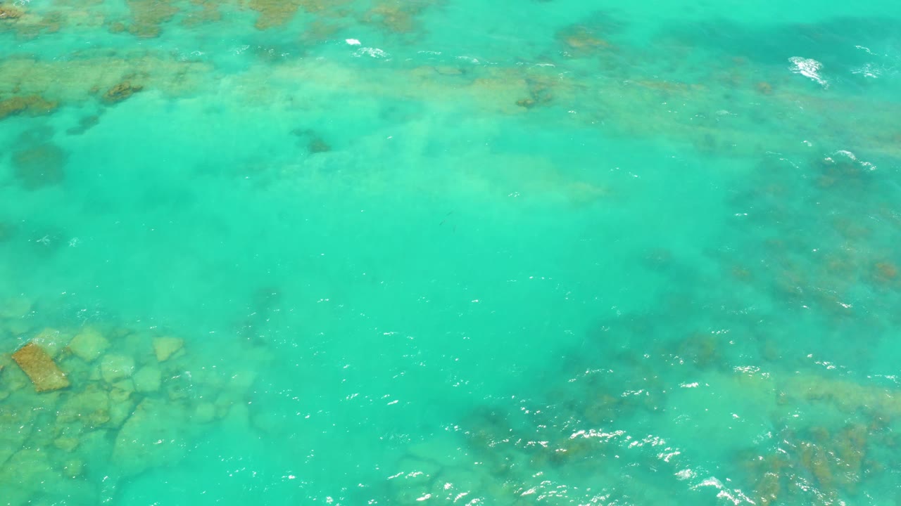 Clear shallow water in Cabo Pulmo, Baja California Sur, with a larger submerged rock cluster entering near the lower left and no visible people.
