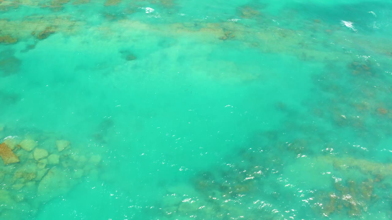 Overhead Cabo Pulmo water detail with faint brown-green seabed patches, scattered white ripples, and no visible people.