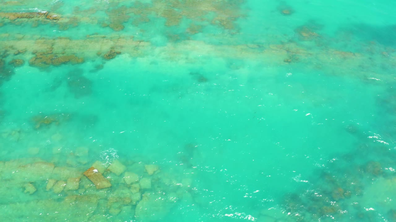 Shallow turquoise ocean water covers scattered rocky patches and coral-like seabed texture in Cabo Pulmo, Baja California Sur, with no visible people.