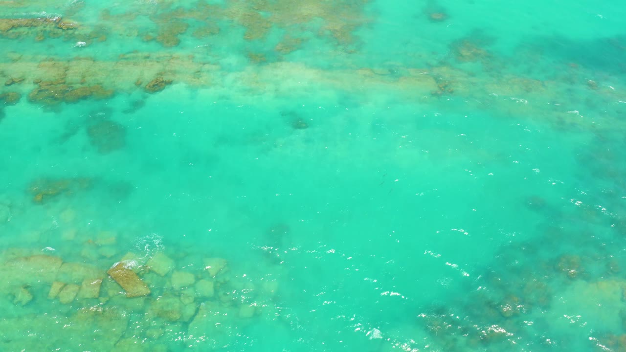 Blue-green water with soft ripples passes over partially visible rocks and sand-toned seabed in Cabo Pulmo, Baja California Sur, with no visible people.