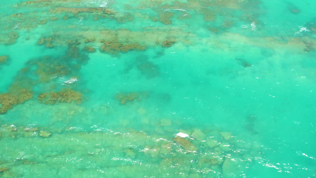 Clear turquoise water in Cabo Pulmo shows submerged rocks crossing the lower part of the frame, with small white ripple highlights and no visible people.