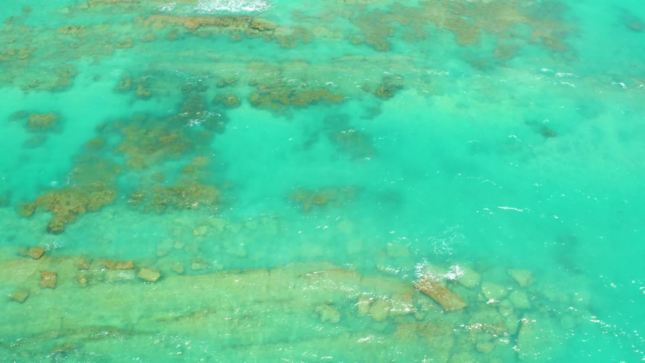 Turquoise Cabo Pulmo water fills the frame with scattered submerged rocks, a lighter bottom band, ripples, a small foam patch near the lower right, and no visible people.