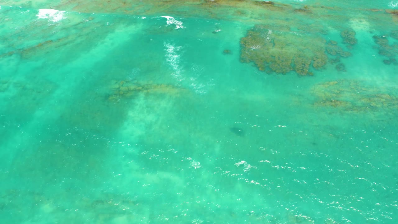 Turquoise ocean surface with pale seabed and reef shapes below.