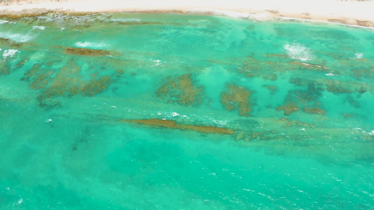 Shallow coastal water with darker reef lines, small waves, and a pale beach strip.