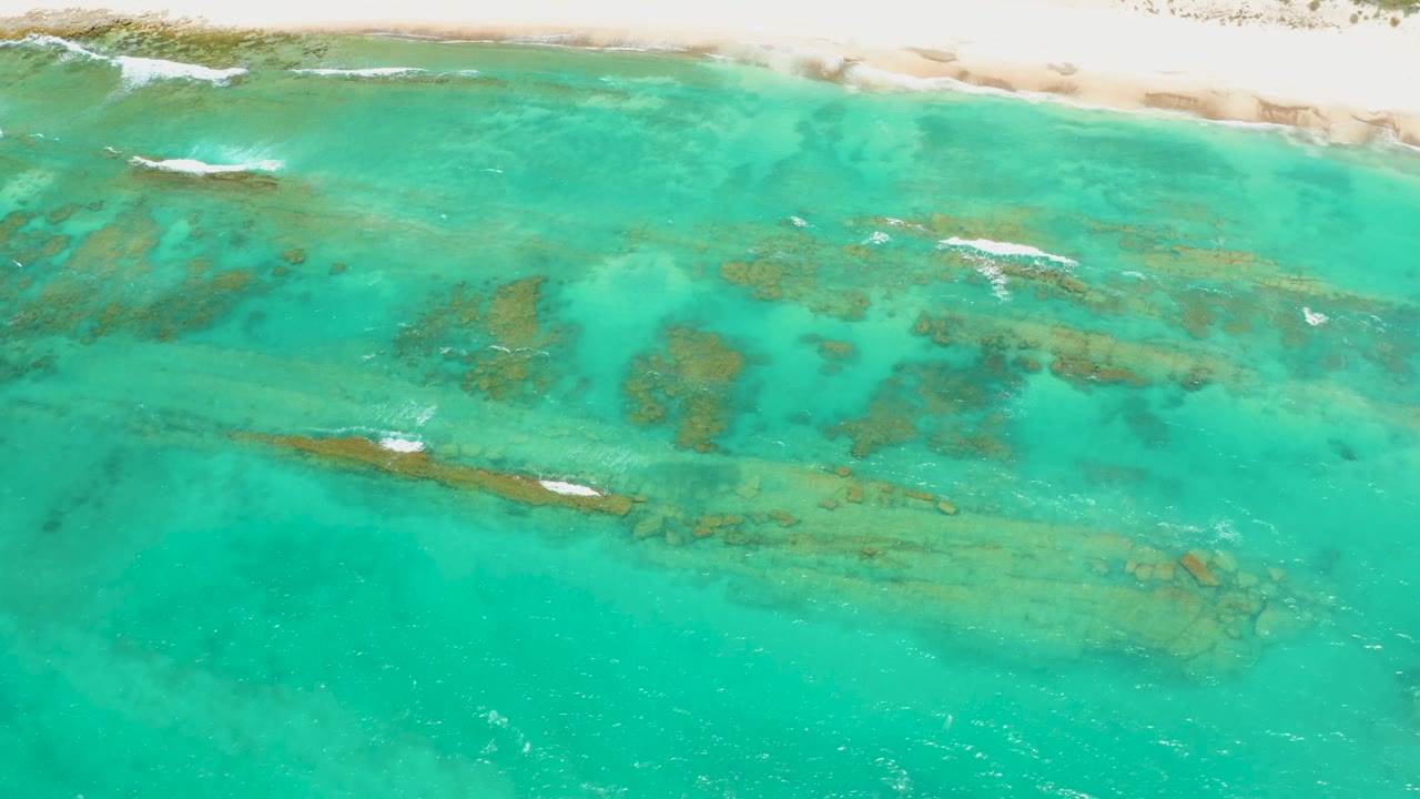 Aerial view of turquoise shallow water over reef near a sandy shoreline.