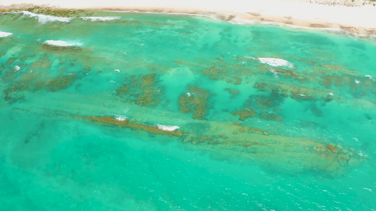 Cabo Pulmo aerial view with coral formations visible through turquoise water, a pale sand strip across the top, and no visible people or boats.