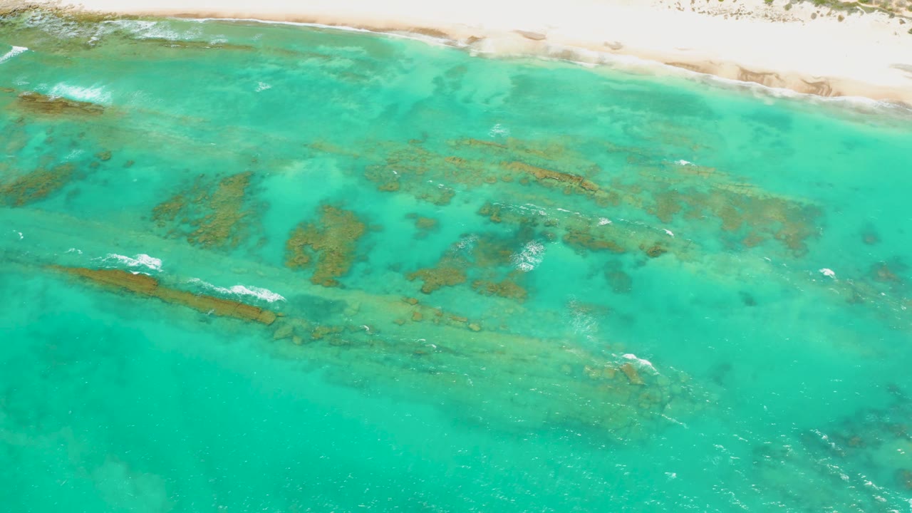 Overhead Cabo Pulmo shoreline frame with pale beach across the top, scattered submerged formations in the center, brighter turquoise water below, and no visible people.