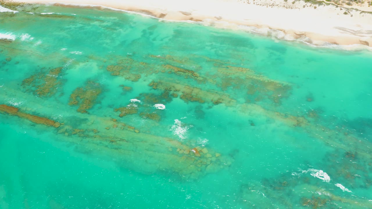 Cabo Pulmo aerial frame with the beach running along the top edge, darker reef patches across the center, and no visible people in the shallow water.