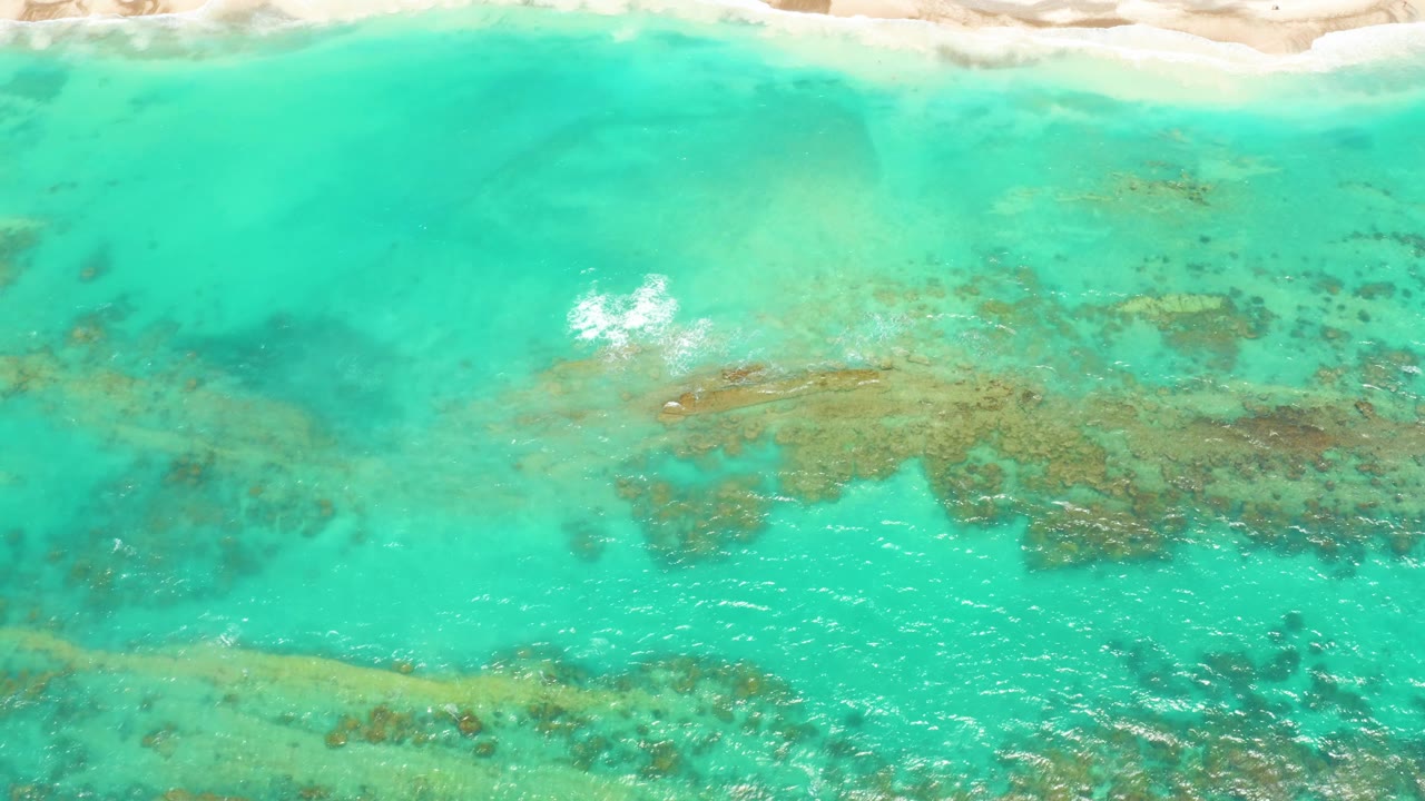 Overhead Cabo Pulmo coastal water with the sandy shoreline along the top, scattered darker underwater patches across the center, and no visible people or vessels.
