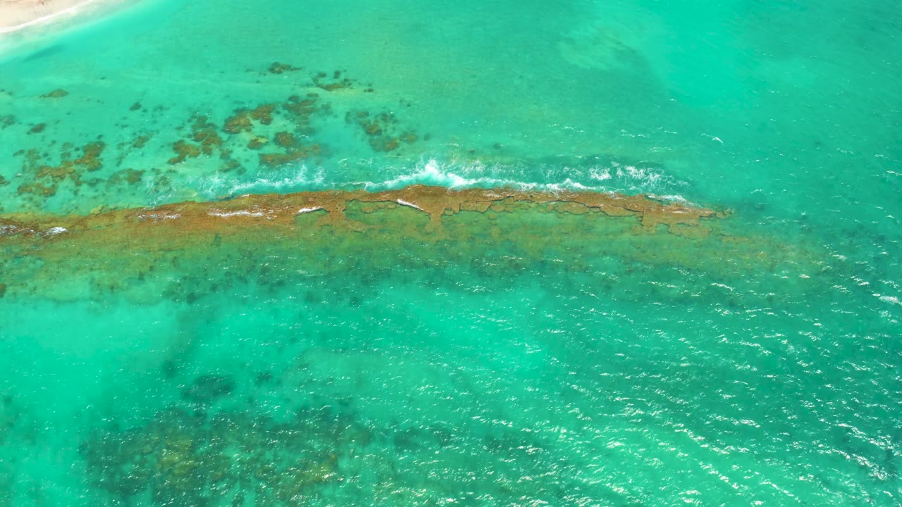 Clear turquoise sea fills the overhead Cabo Pulmo view, with a narrow reef band, small white surf breaks, and no visible people in the water.