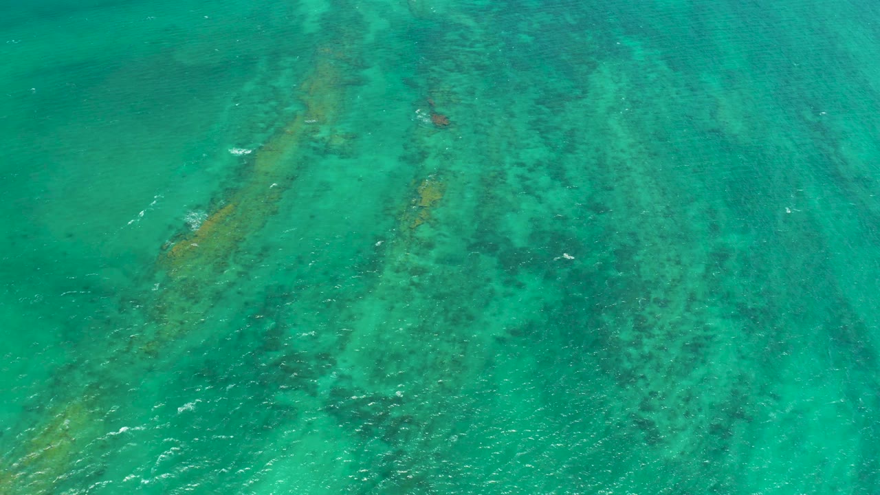 Turquoise water over dark coral and rocky seabed patches.