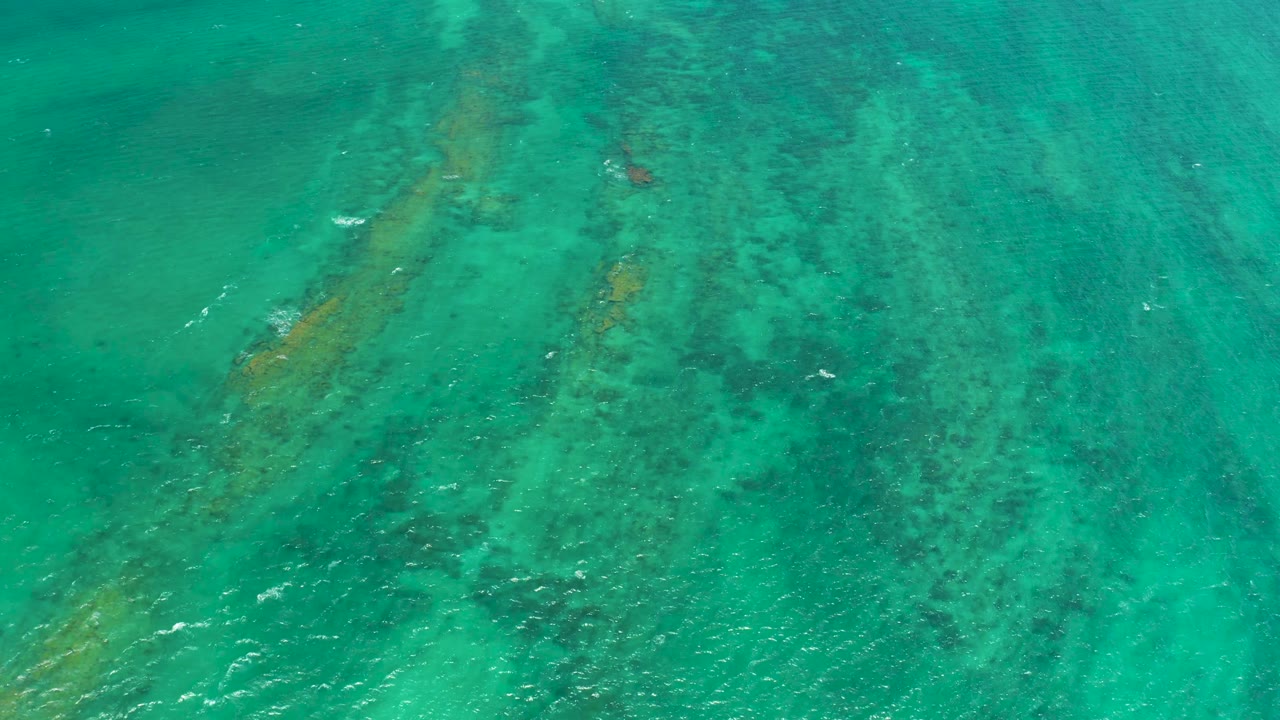 Clear green-blue water in Cabo Pulmo, Mexico, shows elongated reef and rock streaks under gentle surface ripples, with no visible people.