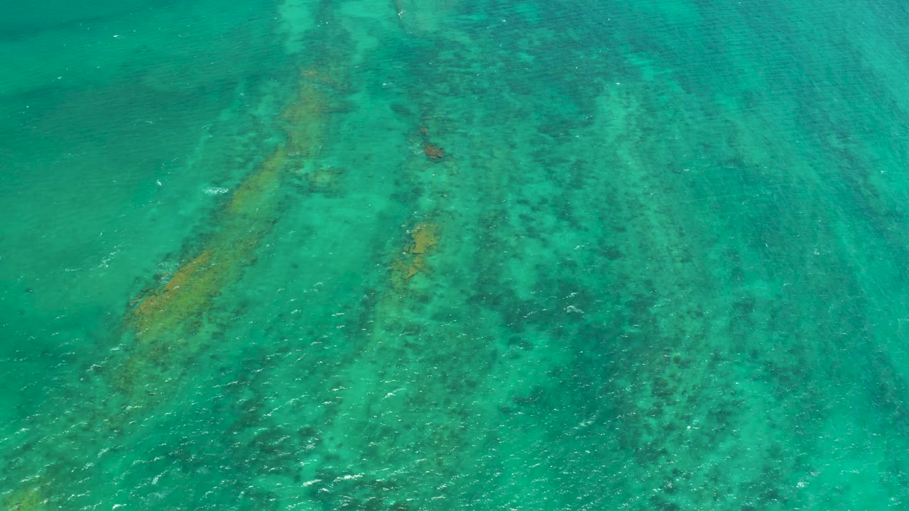 Turquoise ocean surface in Cabo Pulmo, Mexico, sits above darker underwater rock clusters and faint coral color, with no visible people or vessels.
