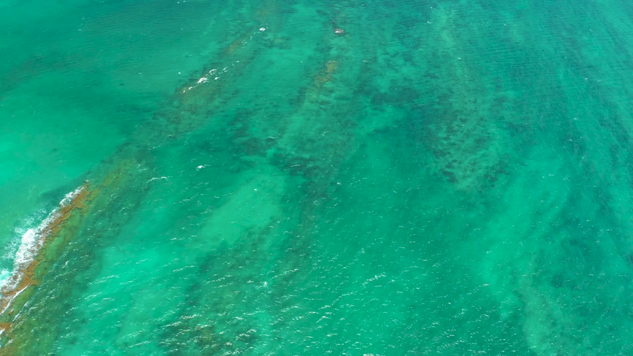 Blue-green water covers diagonal reef forms in Cabo Pulmo, with faint white surface ripples and no visible people.