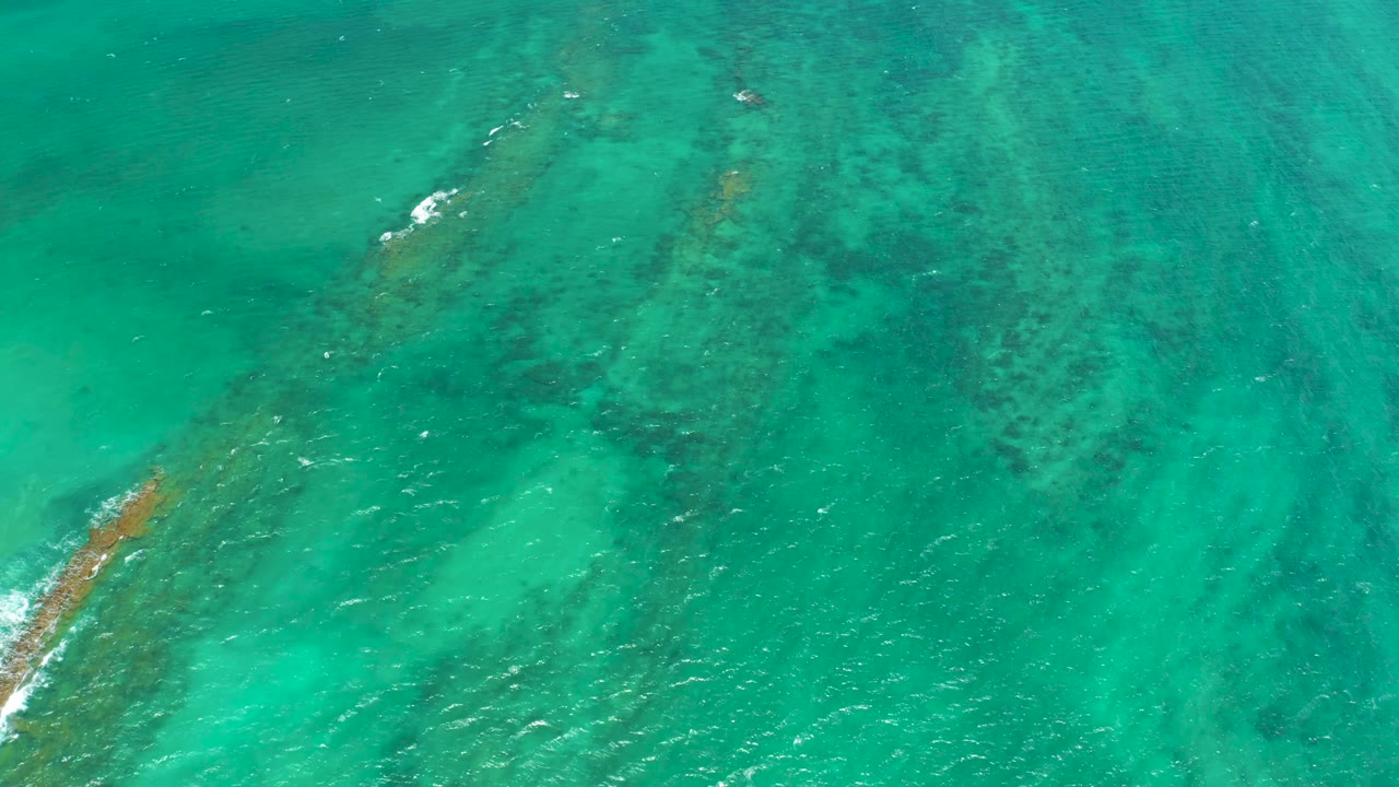 Clear Cabo Pulmo water fills the frame as a reef patch extends from the lower left under the surface, with no visible people.