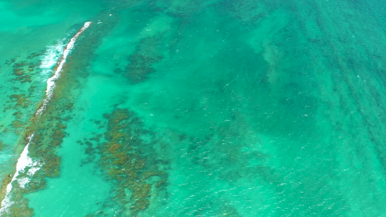 Turquoise shallow water with a diagonal reef line and breaking foam.