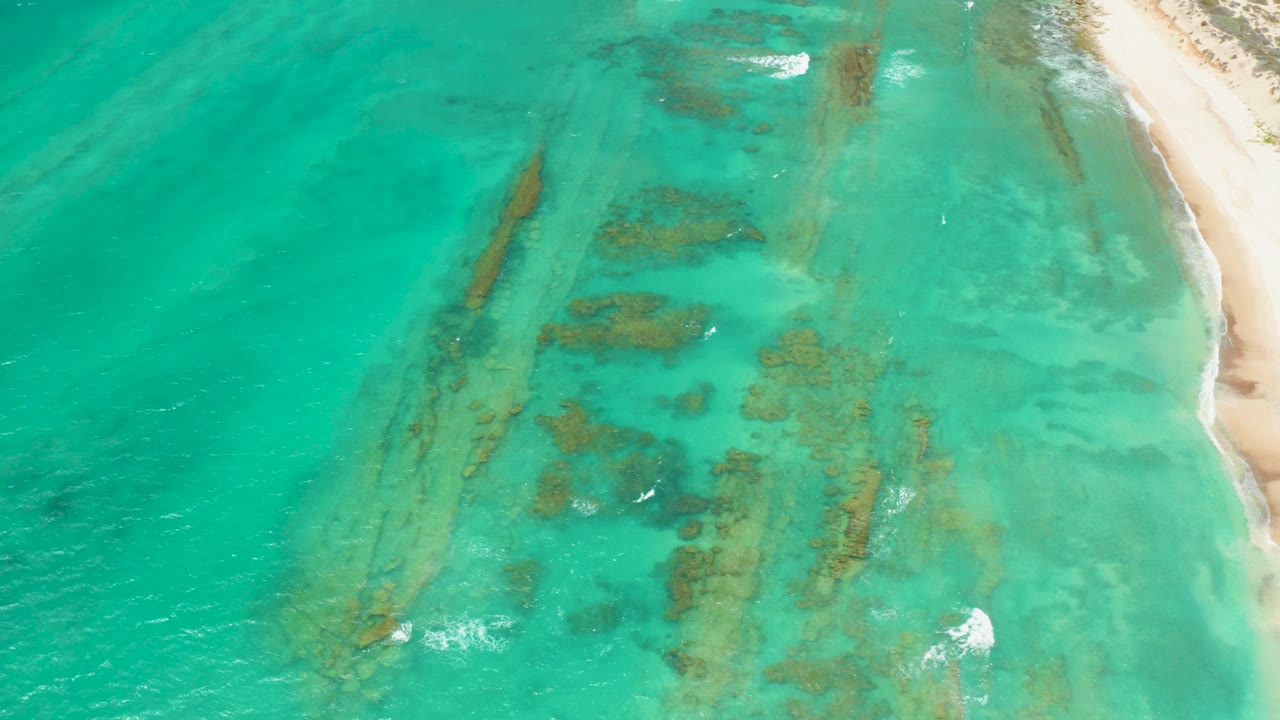 High aerial view of Cabo Pulmo turquoise water with dark submerged formations near a pale sandy shoreline and no visible people.